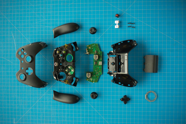Vue à plat des composants internes d'une manette de jeu complètement démontée sur un tapis de découpe.