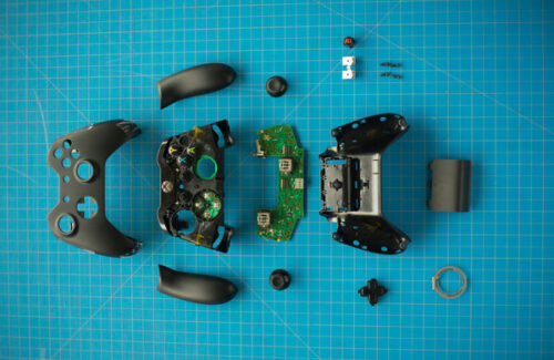 Vue à plat des composants internes d'une manette de jeu complètement démontée sur un tapis de découpe.